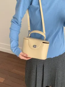 Cream-colored square handbag with top handle and silver buckle worn by a model