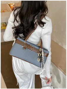Detail view of denim Boston bag with leather belt accents and chain charm accessory