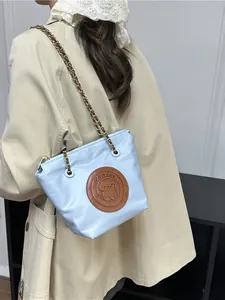 Sac fourre-tout bleu clair en nylon avec chaîne dorée et logo chien porté sur un trench