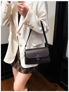 Detailed view of deep brown leather crossbody bag styled with a white blazer outfit