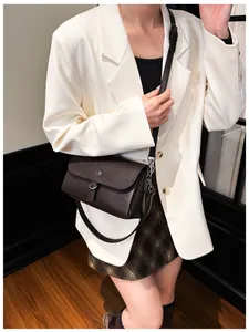 Close-up of a dark brown leather crossbody bag with silver buckle on a model in urban suit