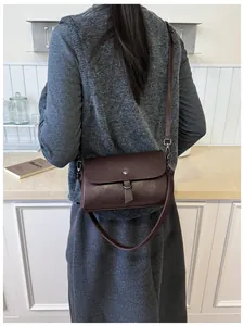Detail of a dark brown matte leather square bag with round metal buckle on a model