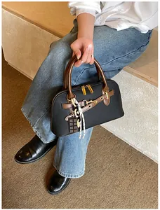 Detail of matte shell bag with brown handles, golden hardware and charm accessories