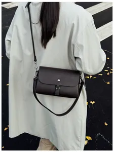 Detail of dark brown leather crossbody bag with silver buckle on a model in autumn setting