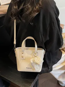 Elegante borsa a secchiello crema con ciondolo a cuore e dettagli dorati ambientata