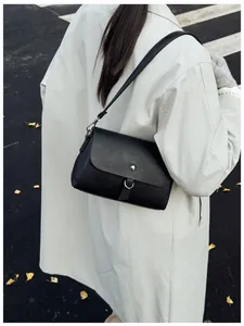 Close-up of black crossbody bag with lychee texture and silver buckle on a beige trench coat