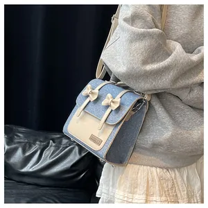 Détail d'un sac bandoulière bleu denim et crème avec nœud décoratif et étiquette tissée