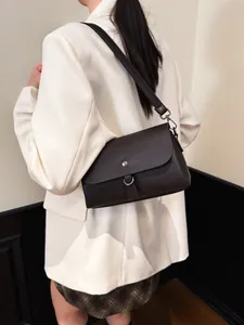 Deep brown lychee texture crossbody bag with silver buckle worn by a model in a beige suit