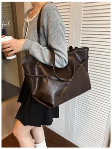 Dettaglio della grande borsa tote marrone scuro con anelli metallici indossata dal modello