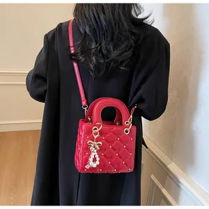 Détail du sac bandoulière rouge matelassé avec rivets étoilés et breloque perle nœud