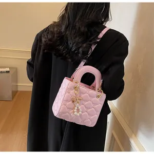 Détail d'un sac à main matelassé rose avec motif cœur, nœud perlé et finitions dorées
