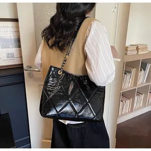 Detail of a large black quilted leather tote bag with elegant gold chain shoulder strap
