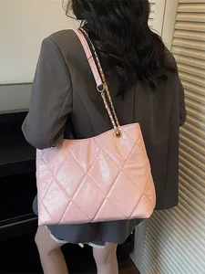 Pink quilted tote bag with woven chain strap shown on a model in grey suit