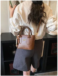 Detail of a brown PU leather bucket bag with cylindrical handles and a wooden bead charm
