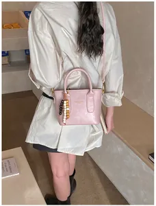 Detail of light pink bucket bag with wooden bead charm and adjustable crossbody strap
