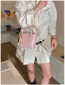 Close-up of pink PU leather crossbody bucket bag with wooden bead charm on a beige shirt
