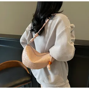 Détail du sac croissant tressé rose nude avec bandoulière nouée et breloque en ambre
