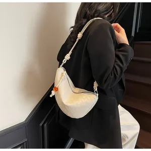 Détail du sac hobo tressé crème avec bandoulière à nœud et perle orange porté par modèle