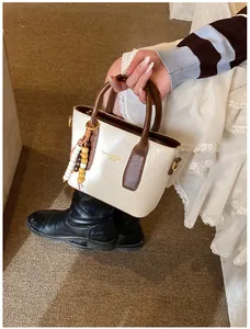 Detail of a chic cream bucket bag with brown handles and a colorful beaded pendant charm