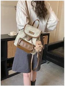 Rear view of a sage green canvas backpack with leather trim and a cute teddy bear charm