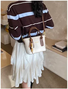 Detail of a chic bucket bag in cream and brown with beaded charm and crossbody strap