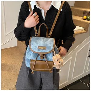 Detail view of blue canvas backpack with leather accents and small bear charm on side