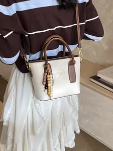Elegant cream leather bucket bag with brown handles and a colorful beaded tassel accessory