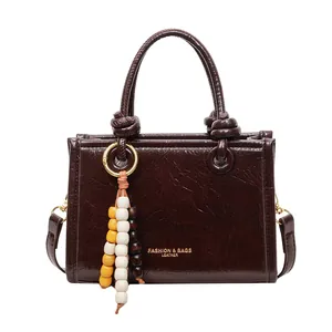 Minimalist dark brown glossy leather handbag with beaded tassel and knot handles