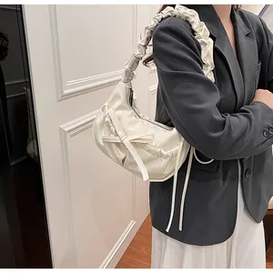 Dettaglio della borsa a tracolla plissettata crema con fiocco decorativo indossata dal modello