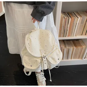 Detail of cream canvas backpack featuring silver star patterns and metallic side buckles
