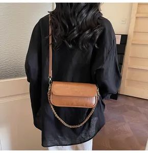 Detailed view of brown baguette bag with brass chain strap and matte leather texture