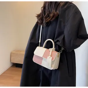 Detail of color-block crossbody bag with top handle and detachable shoulder strap on model