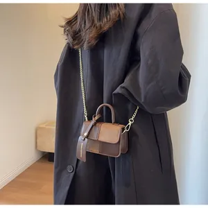Detail of a vintage-style brown leather crossbody bag with gold chain strap on black coat