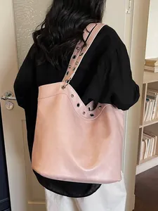 Large pale pink tote bag with metal eyelet straps worn by a model in a minimal room