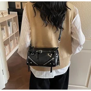 Detail of black glossy faux leather baguette bag with metal zippers and buckles on model