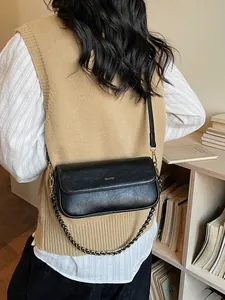Vintage black baguette bag with dual straps and metal chain shown in a warm indoor setting