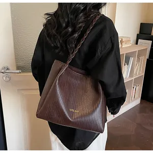 Détail d'un sac cabas marron en cuir tressé avec des anses cylindriques à l'épaule