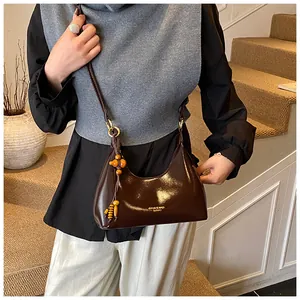 Detail of dark brown patent leather shoulder bag with decorative wooden beads and gold zipper