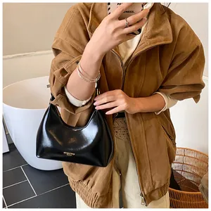 Detail of black glossy shoulder bag with gold lettering held by a model in a brown jacket