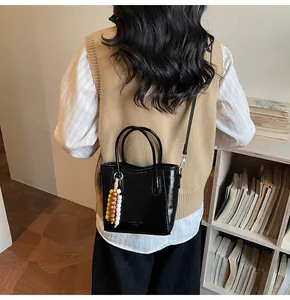 Detail einer schwarzen Lackleder-Beuteltasche mit buntem Perlenanhänger und feinem Riemen