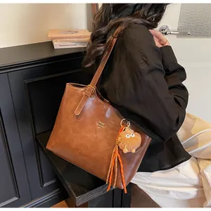 Detail of brown vintage tote bag with gold logo, adjustable strap and plush charm