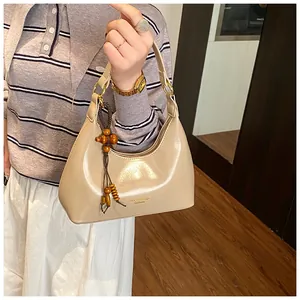 Detailed close-up of a beige hobo bag with a wooden bead charm and gold-toned zipper