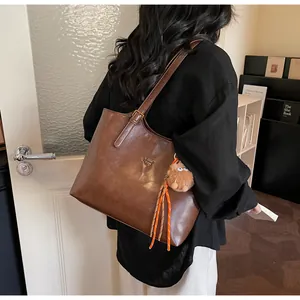 Detailed view of brown leather tote bag with metal logo and plush monster charm decoration