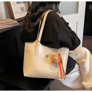 Close-up of beige tote bag with metallic logo and cute plush monster pendant accessory