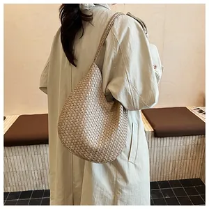 Elegante beige geflochtene Hobo-Umhängetasche mit minimalistischem Trenchcoat in einem Raum