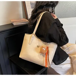 Detail of beige tote bag with cute plush monster charm and orange braided rope accent