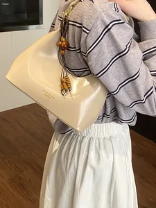 Minimalist beige dumpling shoulder bag for women with wooden bead charm and sleek finish