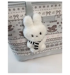 Detail of cute white plush bunny charm with striped scarf on a grey leather tote bag