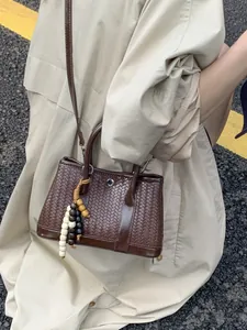 Bruine gevlochten crossbodytas met houten kralen gedragen bij een beige trenchcoat