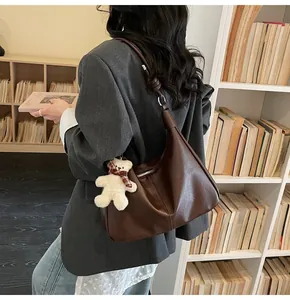 Detail of coffee brown leather crescent bag with knot strap and plush bear charm